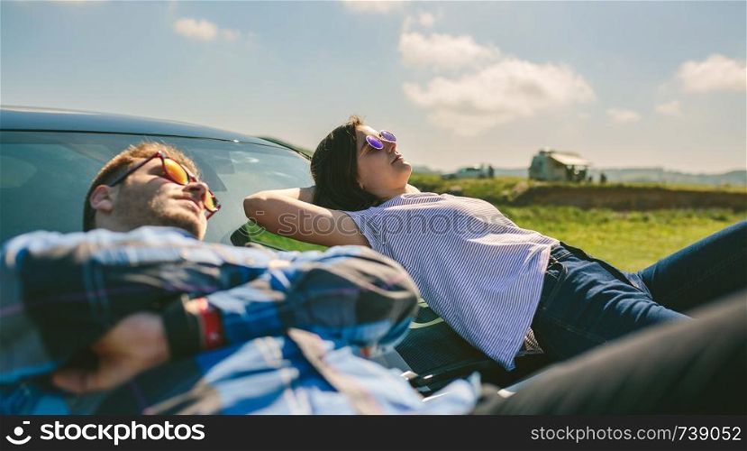 Young couple resting lying on the windshield and the hood of the car. Young couple lying on the windshield