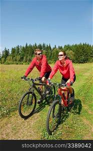 Young couple riding mountain bike in spring meadow nature on sunny day