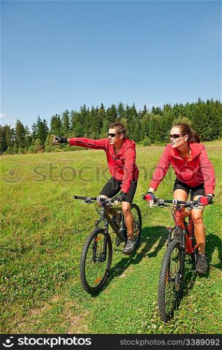 Young couple riding mountain bike in spring meadow nature on sunny day