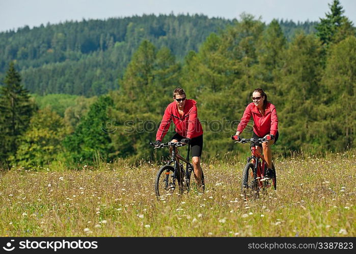 Young couple riding mountain bike in spring meadow on sunny day