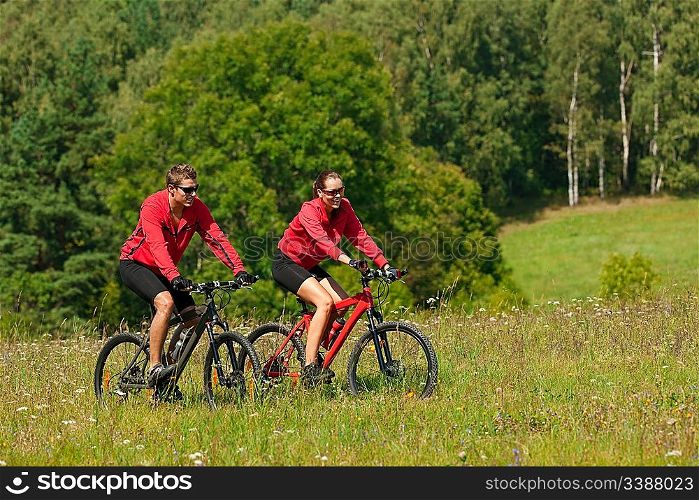 Young couple riding mountain bike in spring meadow on sunny day