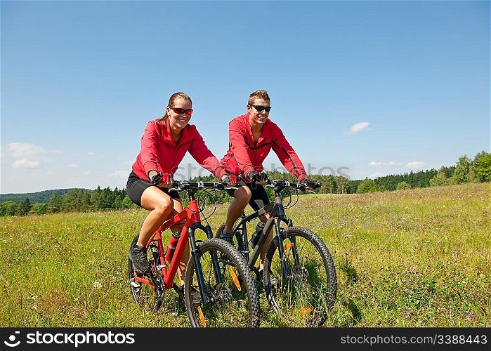 Young couple riding mountain bike in spring meadow on sunny day