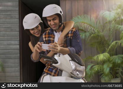 Young couple riding on a motorbike using mobile phone