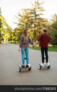 Young couple riding on gyro board in park, back view. Outdoor recreation with electric gyroboard. Transport with balance technology