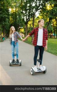 Young couple riding on gyro board in park. Outdoor recreation with electric gyroboard. Transport with balance technology