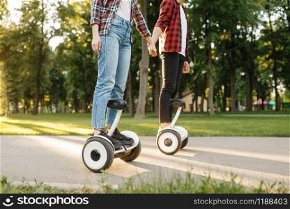 Young couple riding on gyro board in summer park at sunset. Outdoor recreation with electric gyroboard. Transport with balance technology, electrical gyroscope vehicle. Young couple riding on gyroboard in park at sunset