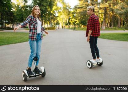 Young couple riding on mini gyro board in summer park. Outdoor recreation with electric gyroboard. Transport with balance technology
