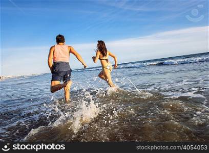 Young couple running in sea, rear view