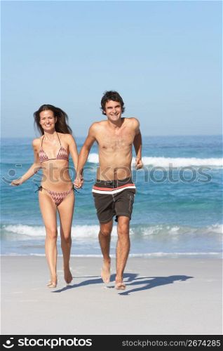 Young Couple Running On Beach Wearing Swimwear