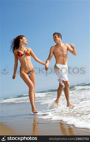 Young couple running through surf on beach, front view
