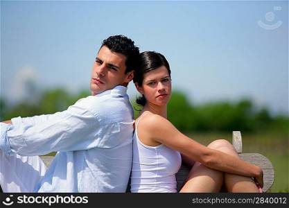 Young couple sat back to back on bench