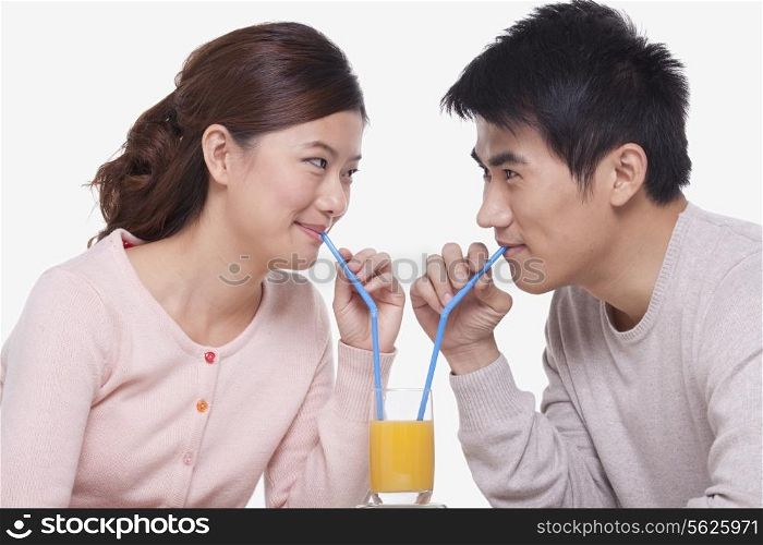 Young couple sharing a glass of orange juice, studio shot