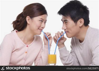 Young couple sharing a glass of orange juice, studio shot