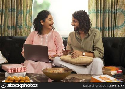 Young couple shopping online through laptop using credit card during festival while sitting on sofa at home