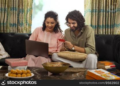 Young couple shopping online through laptop using credit card during festival while sitting on sofa at home
