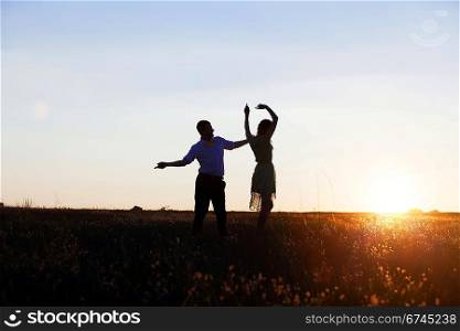 Young couple silhouettes dancing on the field at sunset