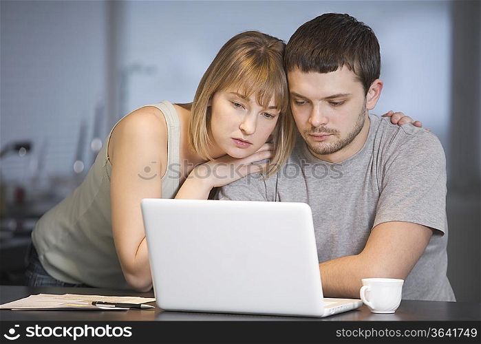Young couple sit at laptop in kitchen