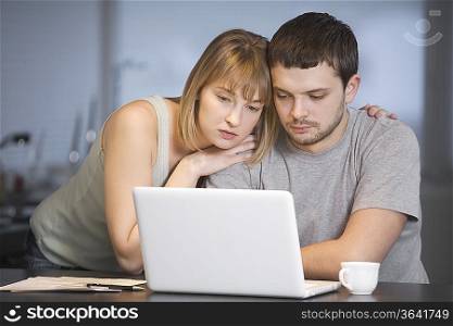 Young couple sit at laptop in kitchen