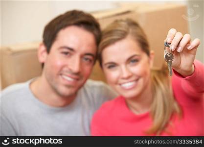 Young couple sit on the floor around boxes holding key in hand