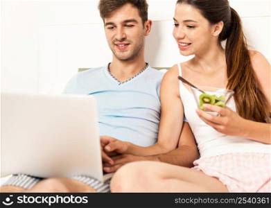 Young couple siting on bed working and eating breakfast