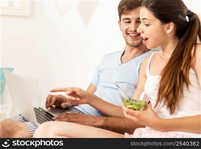 Young couple siting on bed working and eating breakfast