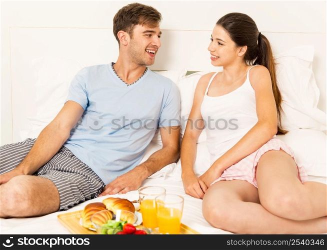 Young couple siting on the bed and ready to eat the breakfast