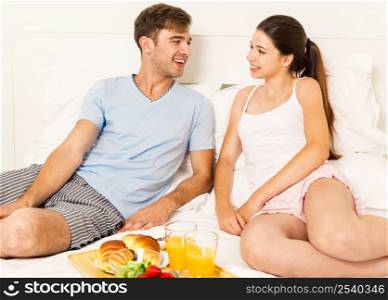 Young couple siting on the bed and ready to eat the breakfast