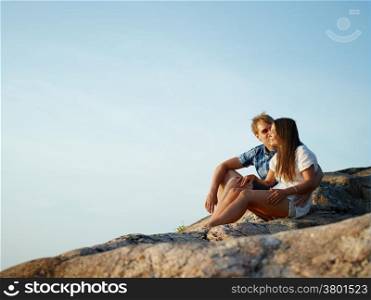 Young couple sits together on the cliff, blue sky on background