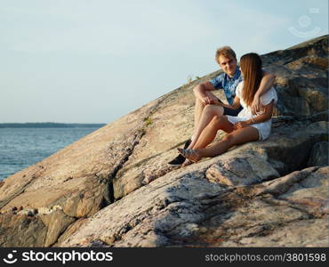 Young couple sits together on the cliff, rocky shore in archipelago