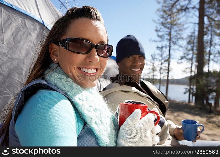 Young Couple sitting at campsite drinking from mugs.