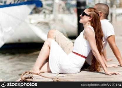 young couple sitting at the wooden boardwalk and looking the sea