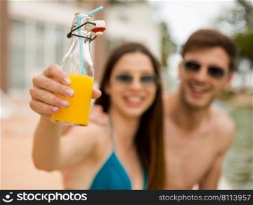 Young couple sitting by the pool and drinking natural juices