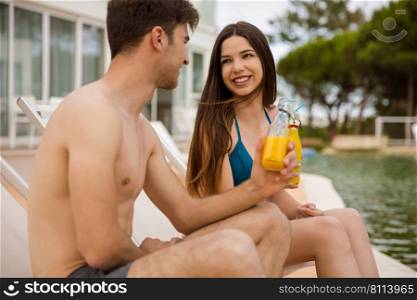 Young couple sitting by the pool and drinking natural juices