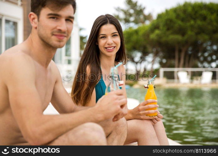 Young couple sitting by the pool and drinking natural juices