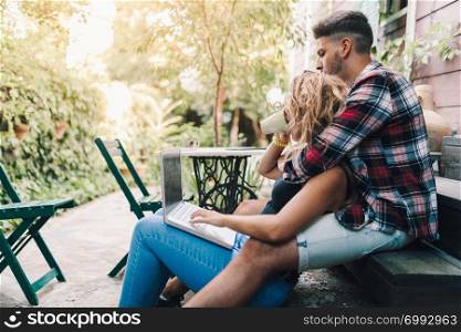 Young couple sitting embraced in the steps of their wooden house with a laptop
