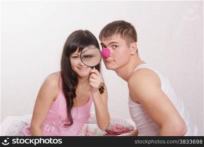 Young couple sitting in bed and having fun with a magnifying glass and clown nose