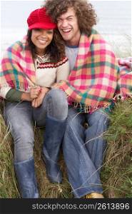 Young Couple Sitting In Sand Dunes Wrapped In Blanket