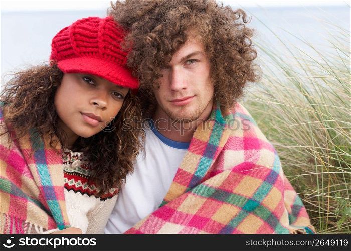 Young Couple Sitting In Sand Dunes Wrapped In Blanket