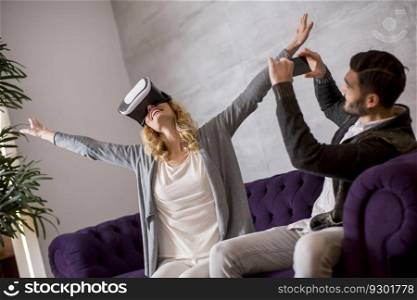 Young couple sitting in the room while young woman wearing a virtual reality glasses