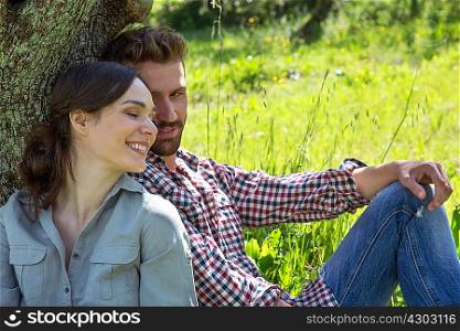 Young couple sitting leaning against tree together
