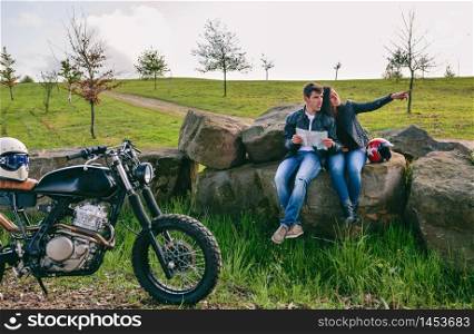 Young couple sitting looking at a map during a motorcycle trip. Couple sitting looking at a map with motorcycle