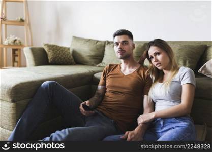 young couple sitting near sofa watching television home