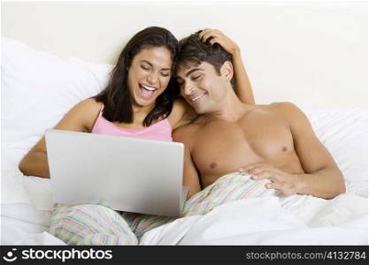 Young couple sitting on a bed looking at a laptop