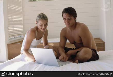 Young couple sitting on a bed working on a laptop