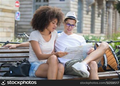 young couple sitting on a bench and checking a map