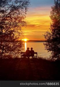 Young couple sitting on a bench by the lake in beautiful golden summer sunset