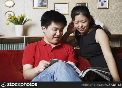 Young couple sitting on a couch reading a magazine