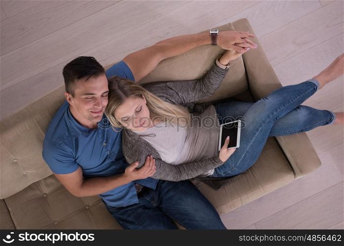 Young couple sitting on a sofa in the luxury living room, using a tablet computer top view