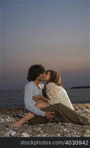Young couple sitting on beach kissing