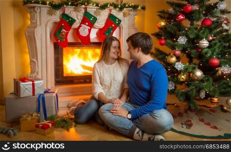 Young couple sitting on floor at burning fireplace and giving Christmas presents
